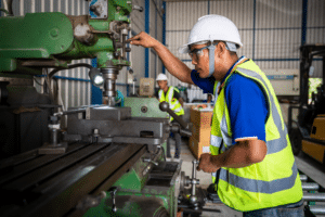 A man in a hard hat operates a machine, emphasizing safety in a manufacturing environment.