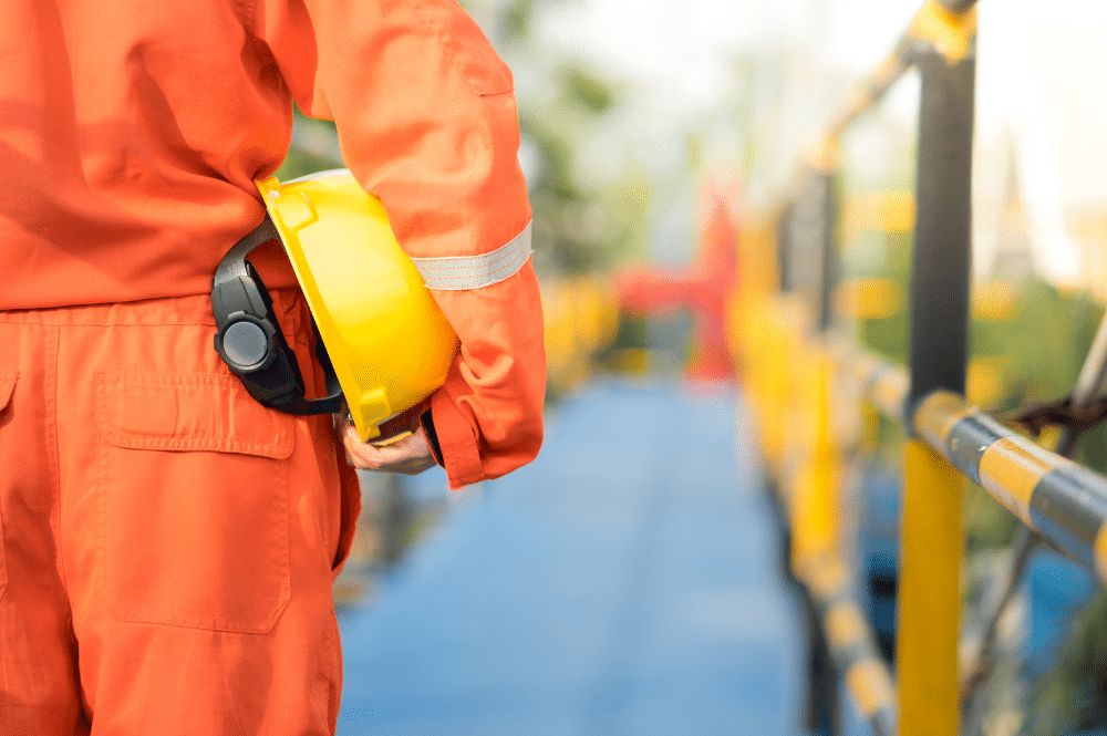 A man in an orange jumpsuit holds a yellow helmet, symbolizing a commitment to a safety culture in the workplace.