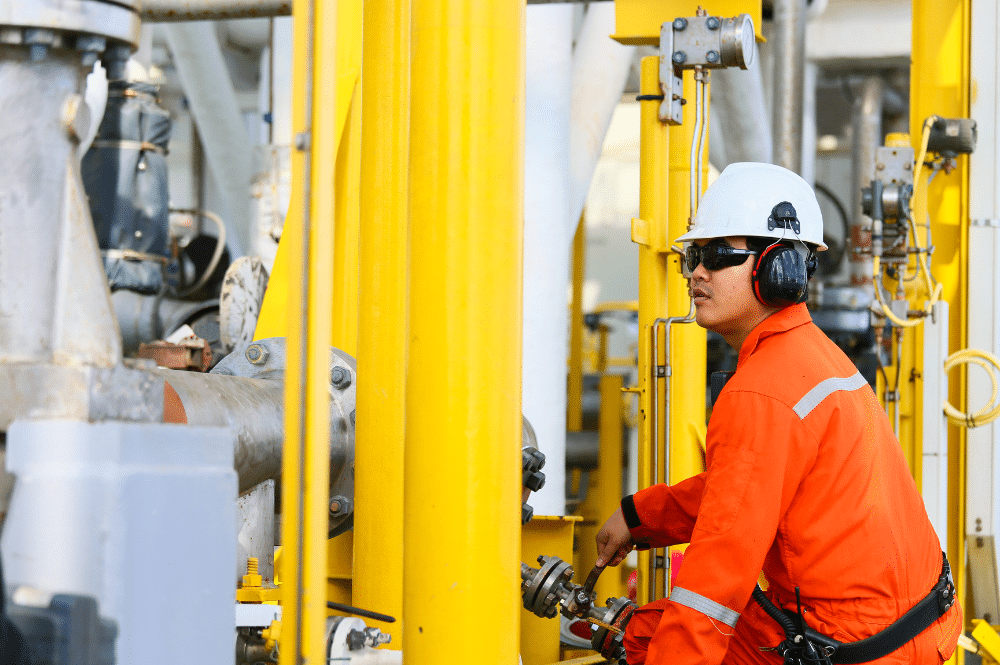 A man in an orange shirt and safety glasses diligently working on a gas pipeline, emphasizing oil and gas safety protocols.